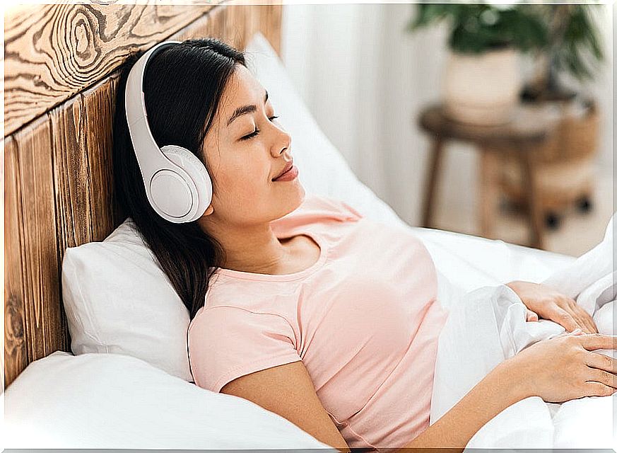 Woman with headphones listening to relaxing music on her bed.